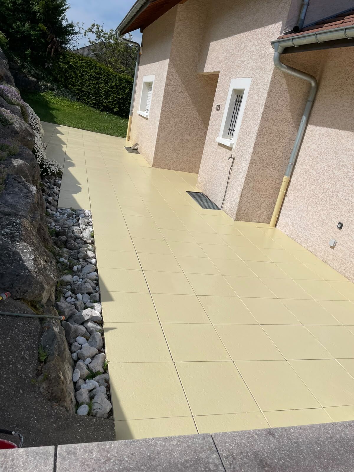Terrasse en dalles repeintes en jaune clair le long d'une maison en Haute-Savoie